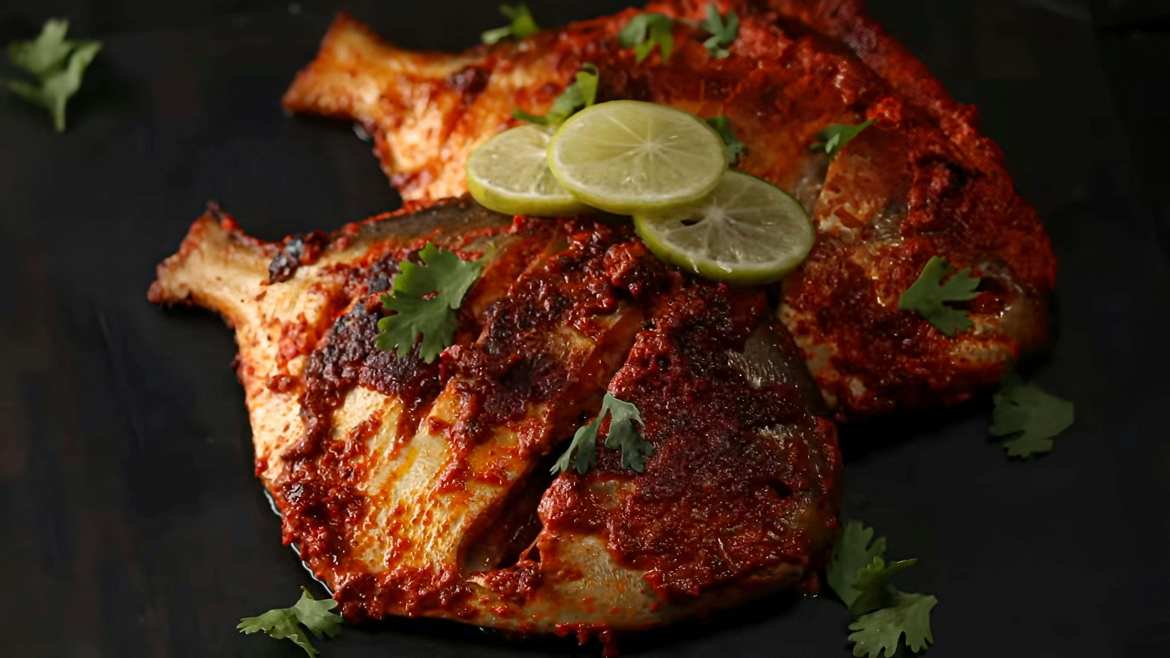 cooked fish with some limes and cilantro all, against a dark background