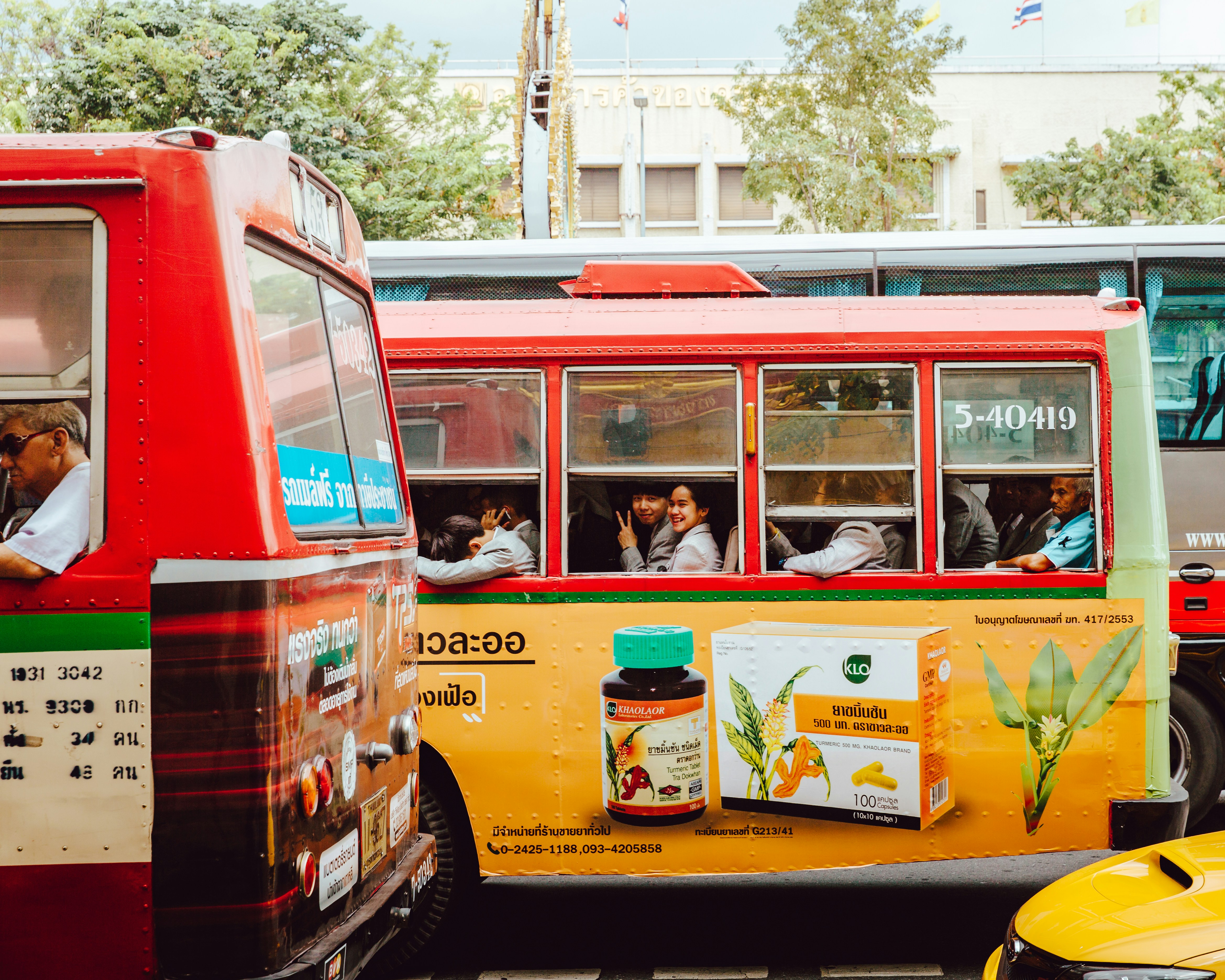 people on red and yellow bus smiling and waving from inside the bus