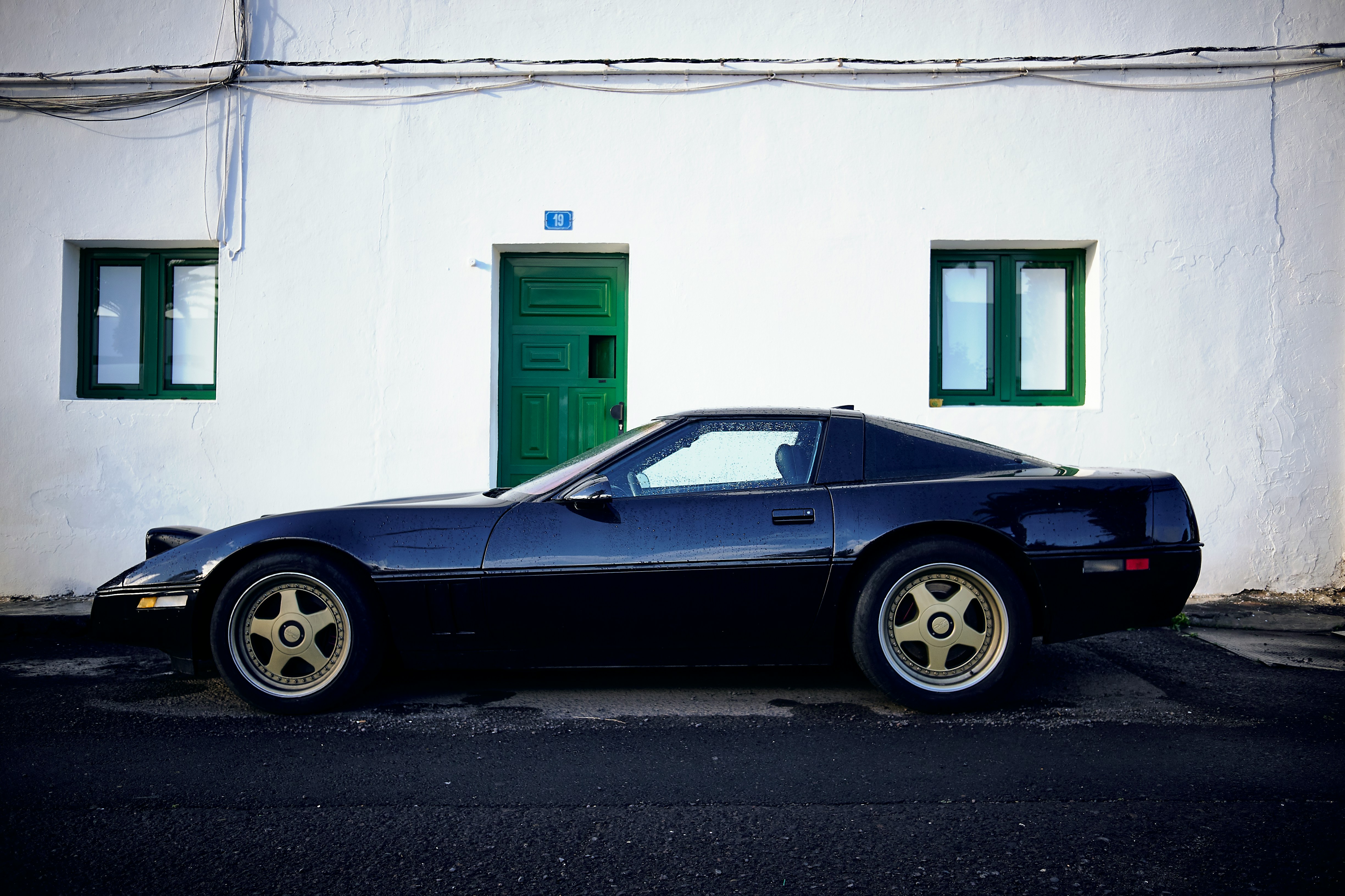 blue car against a white building with green doors and green window frames